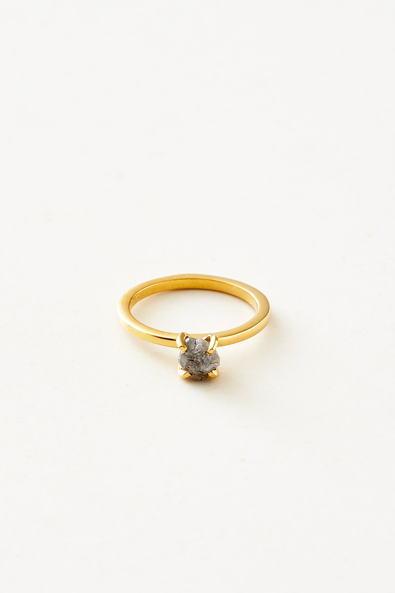 En guldring med en rå, grå diamant er centreret på en hvid baggrund. Ringen er enkel og elegant.