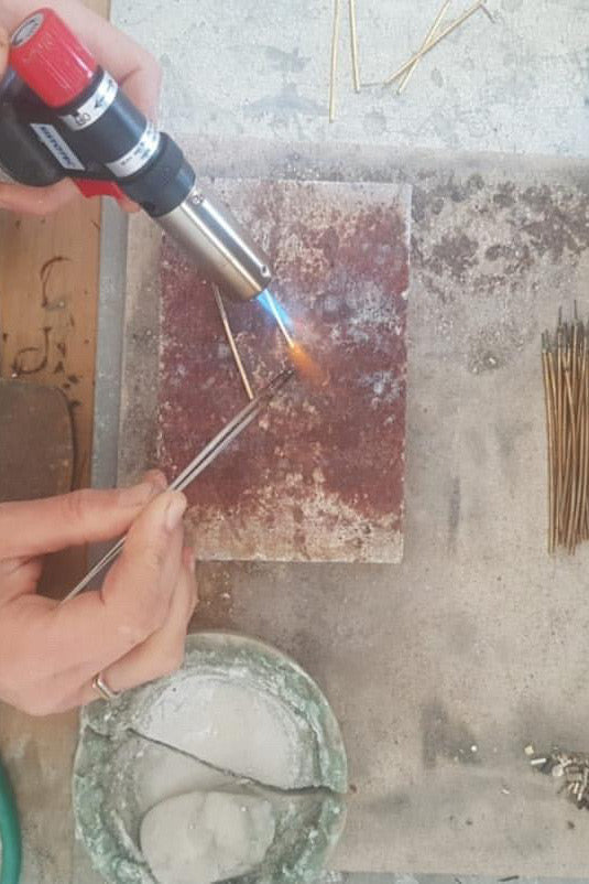 En gasbrænder opvarmer en metaltråd, der holdes med en pincet, over en brandsikker mursten. En skål med pasta er placeret tæt på.