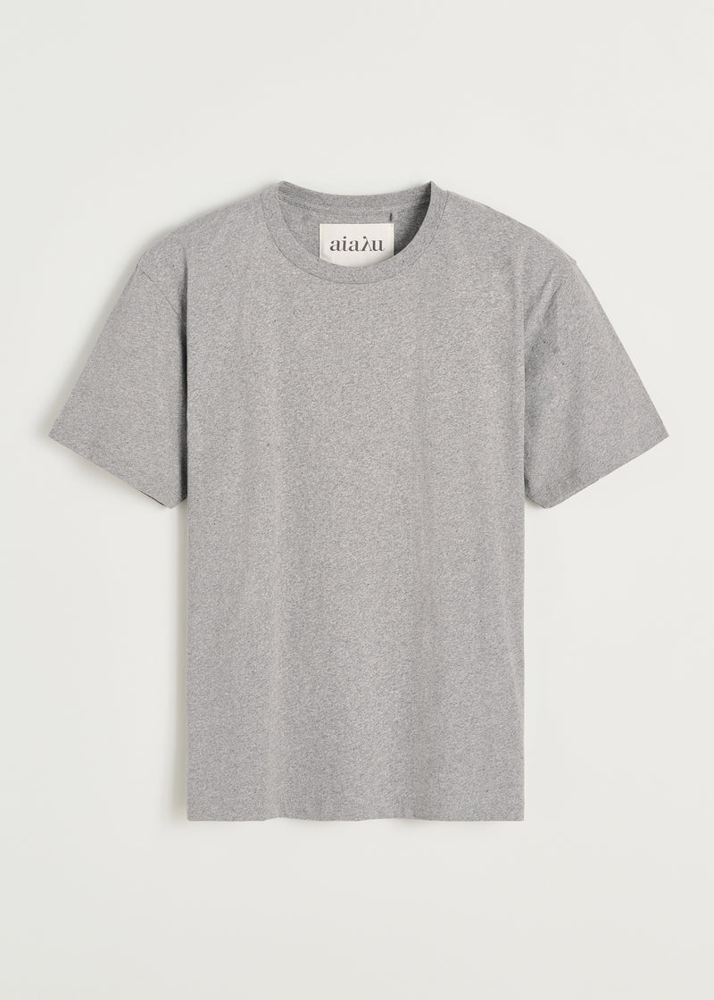 En grå T-shirt, med teksten "aiaλu" på indersiden af kraven, ligger fladt mod en hvid baggrund.