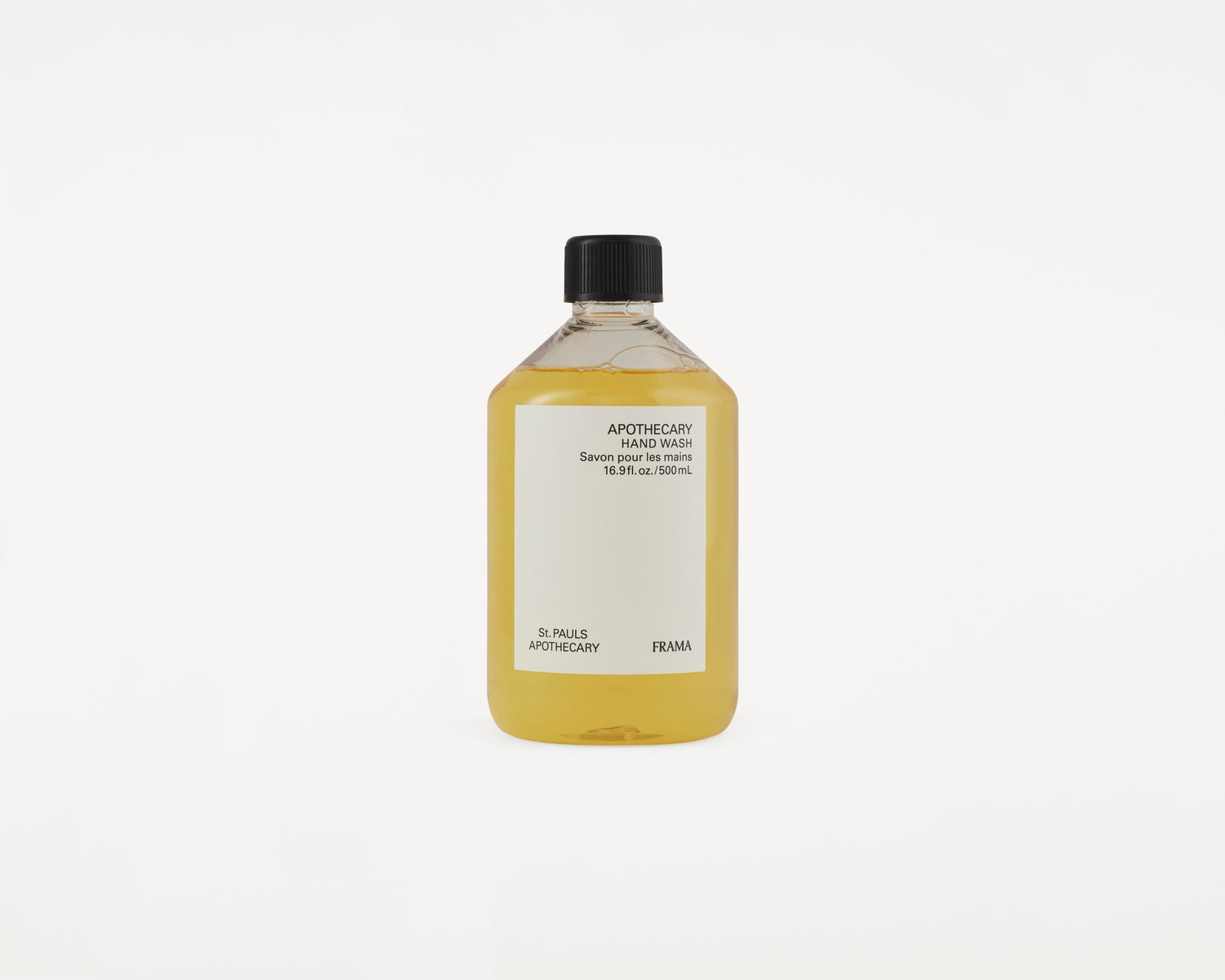 En flaske med gullig flydende håndsæbe står. Etiket tekst: "APOTHECARY HAND WASH Savon pour les mains 16.9fl.oz./500mL St. PAULS APOTHECARY FRAMA". Baggrund er hvid.