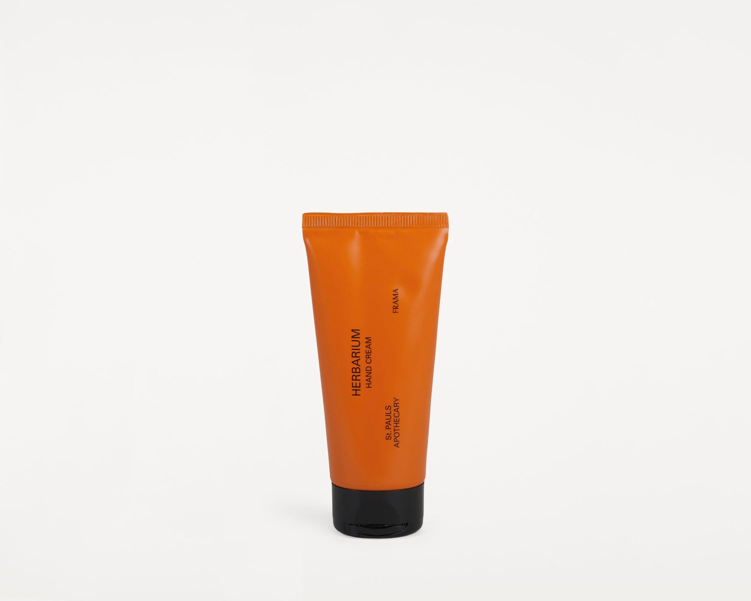 En orange tube "Herbarium Hand Cream", fra "Frama St. Pauls Apothecary", står oprejst på en hvid overflade.