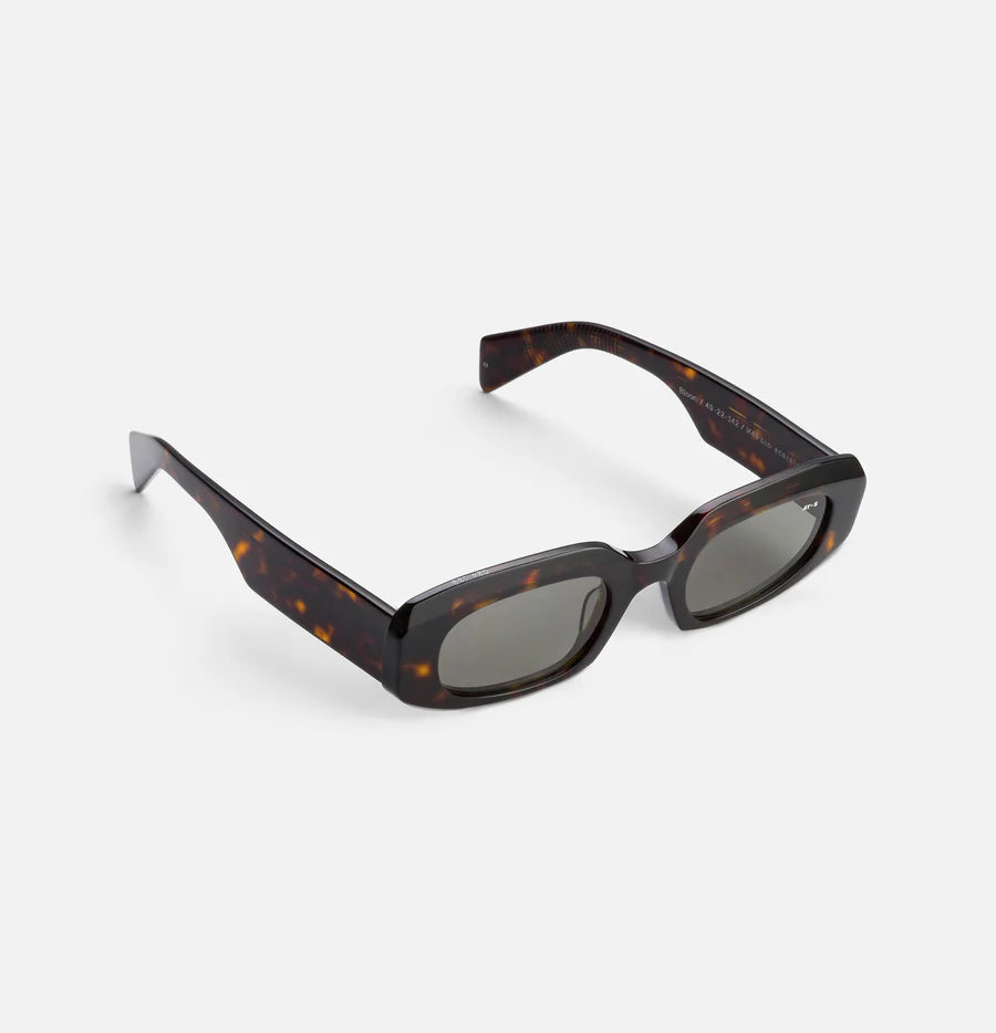 Firkantede, mørk-skildpaddemønstrede solbriller ligger diagonalt på en hvid overflade. Teksten på brillestangen er "Bison 7 49-22-142 F MADE IN ITALY".