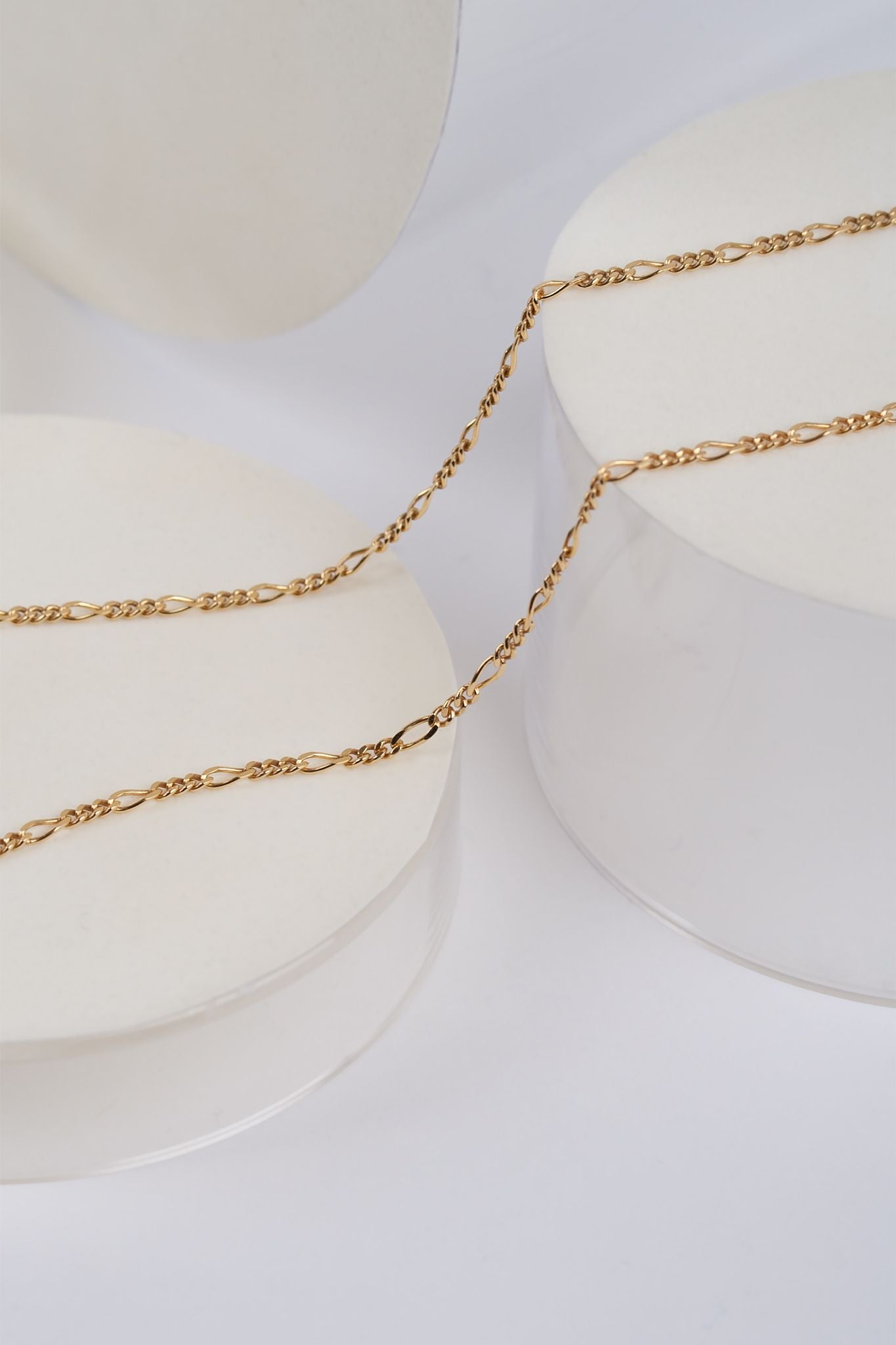 En guldkæde snor sig over hvide, runde piedestaler i en lys baggrund.