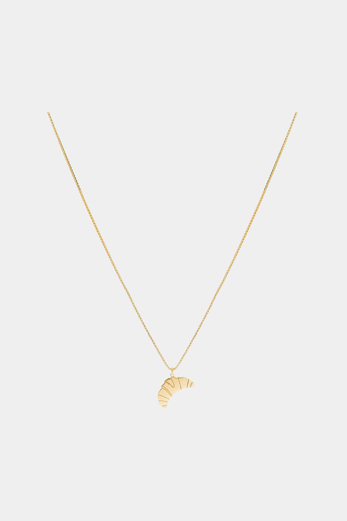 En guldkæde hænger nedad med et croissant-vedhæng nederst, vist mod en ren, lysegrå baggrund.