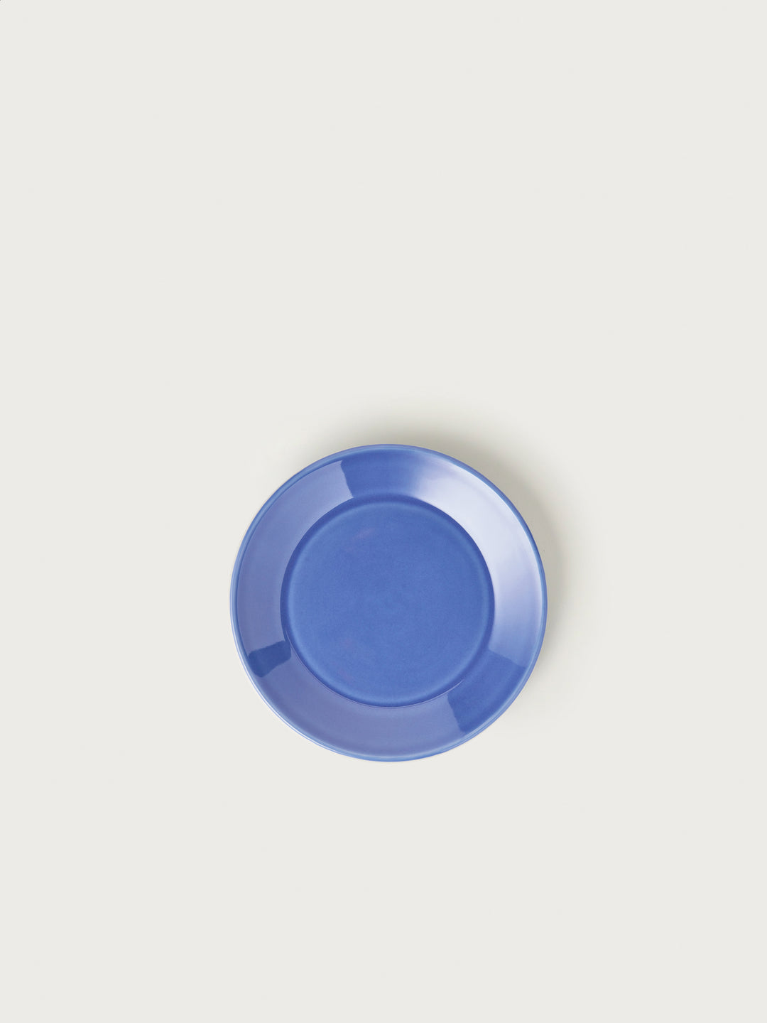 En blå tallerken ligger centralt på en ensfarvet, beige baggrund. Tallerkenen er tom.