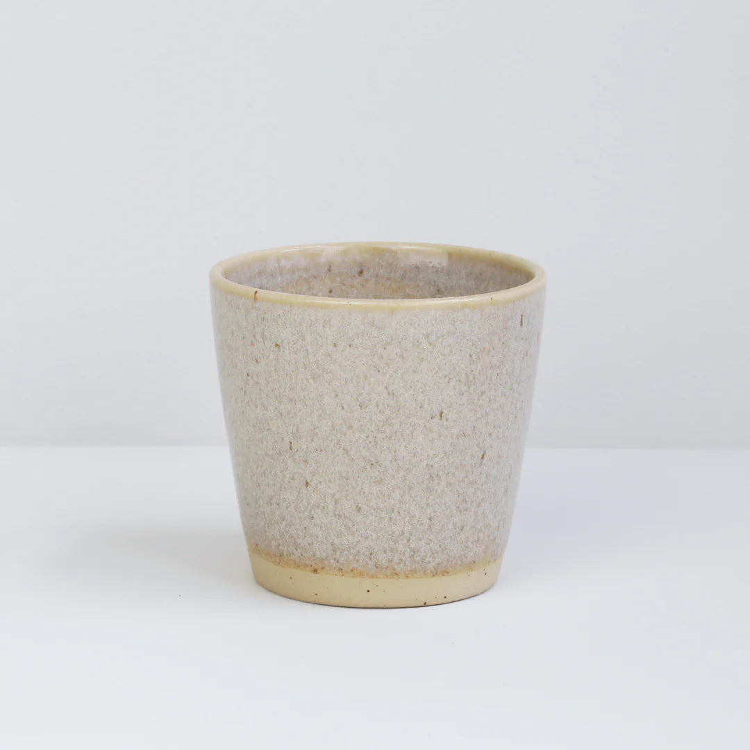 En keramisk kop står stille. Koppen har en beige, spættet overflade og er placeret på en hvid baggrund.