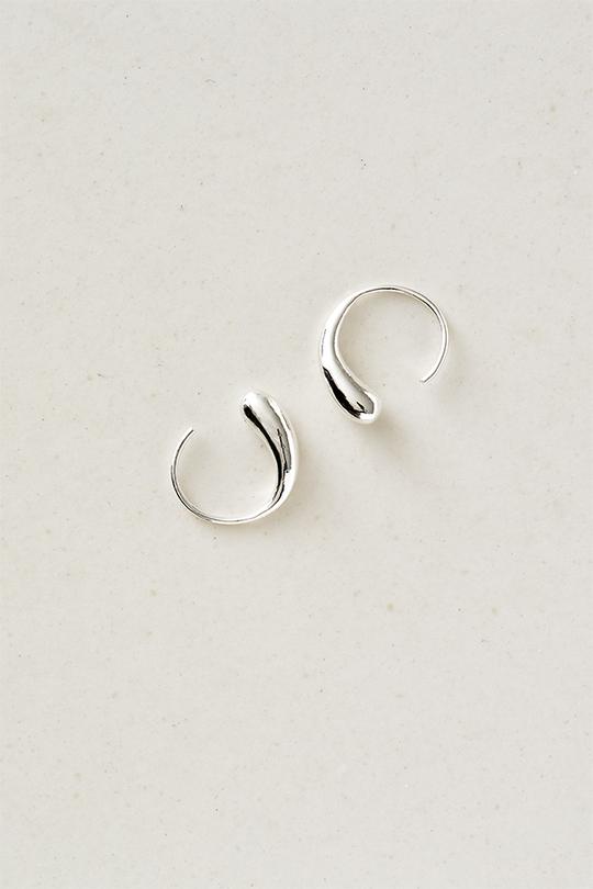 To sølvfarvede øreringe ligger på en lys, jævn overflade. De er formet som dråber med en åben cirkel i bunden.