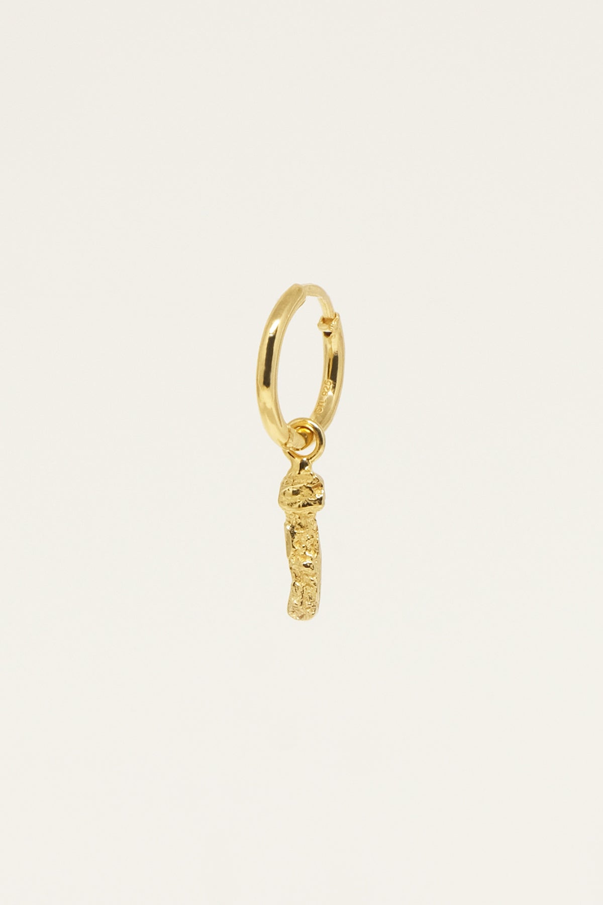 En enkelt, guld ørering hænger på en beige baggrund. Den har en tynd, cirkelformet bøjle med en lille, uregelmæssig guld vedhæng der dingler ned fra den. Der står "CE 925" på bøjlen.
