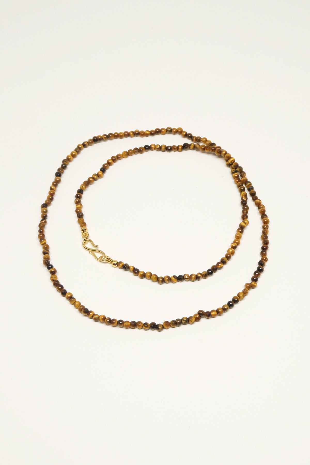 En halskæde af tigerøjeperler ligger snoet på en hvid baggrund. Den har en guldfarvet lås.