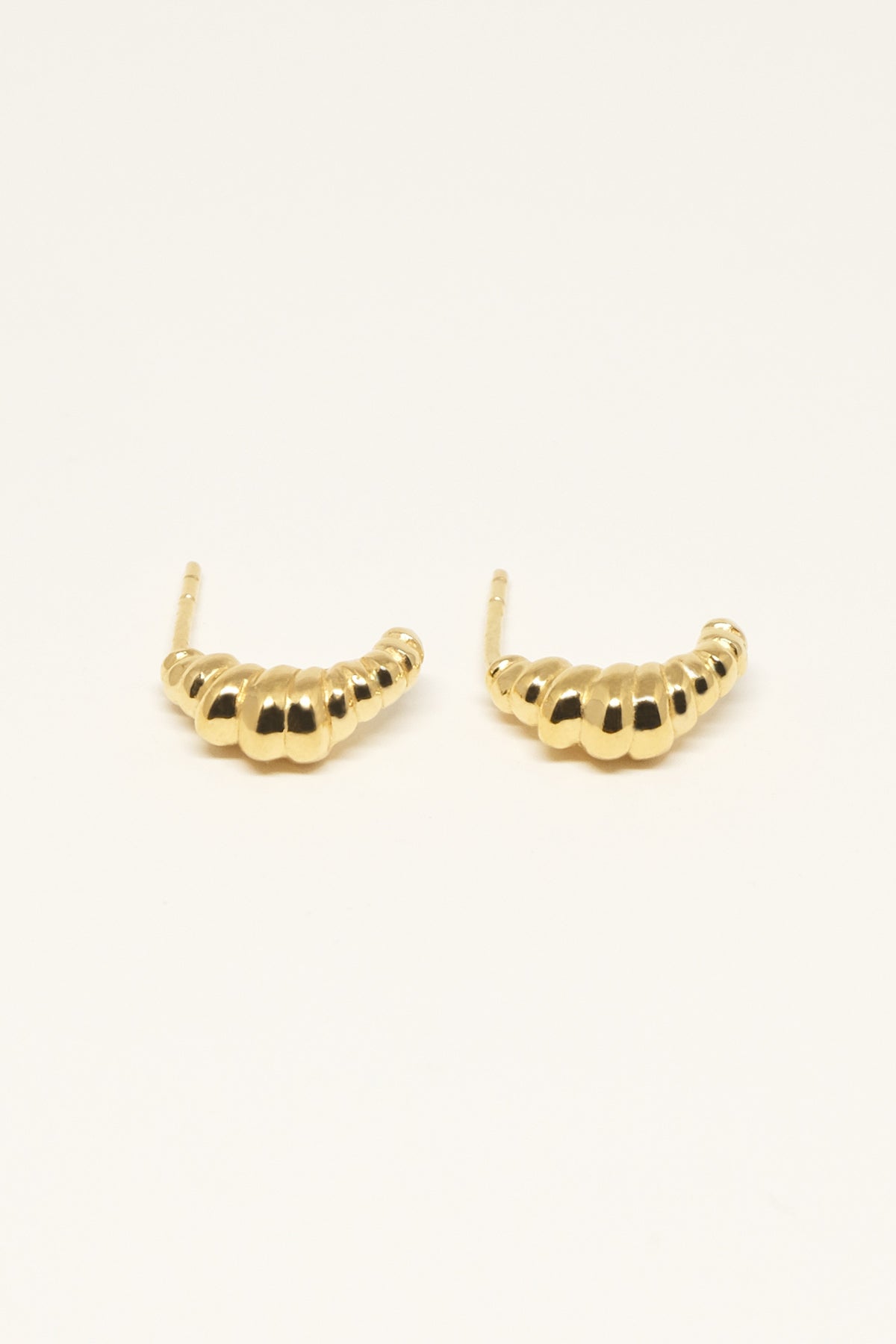 To guldøreringe, formet som buede rækker af små kugler, ligger ved siden af hinanden på en hvid baggrund.