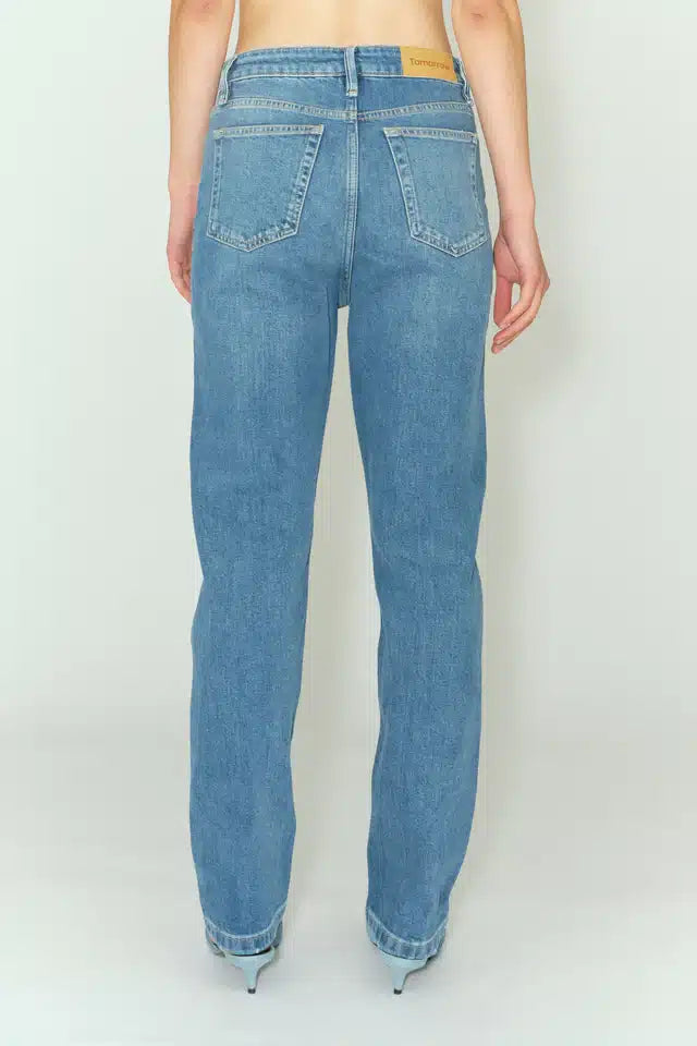 Personen står, iført lyseblå jeans og lyseblå sko med hæl mod en hvid baggrund. Et mærke med ordet "Tomorrow" kan ses bag på jeans.