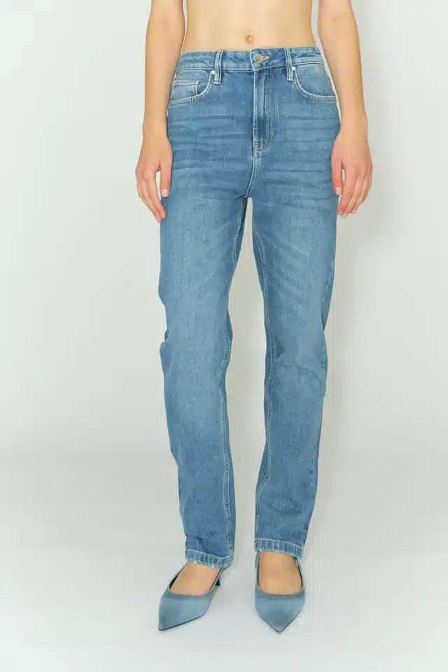 En person står iført lyseblå jeans og blå sko med hæle. Baggrunden er hvid og neutral.