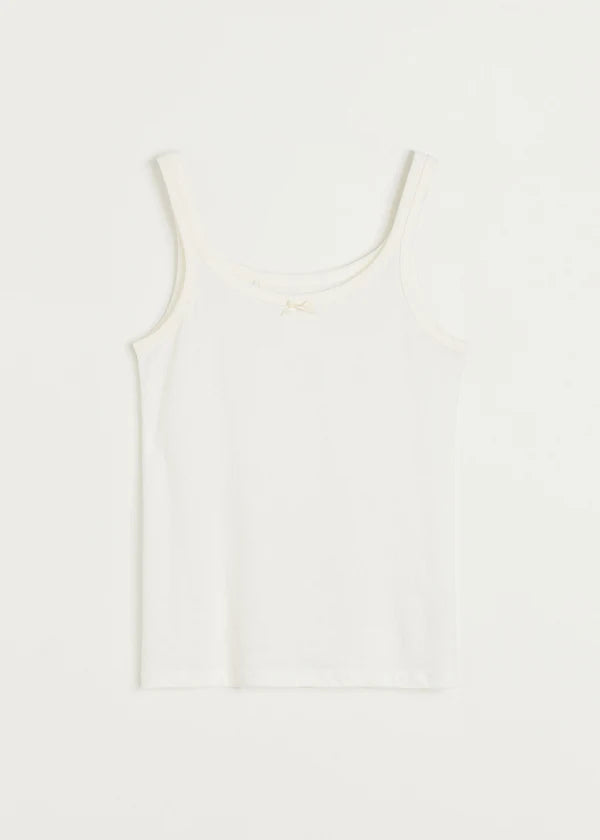 En hvid tanktop med tynde stropper ligger fladt på en hvid baggrund. Den har en lille sløjfe i midten af halsudskæringen.