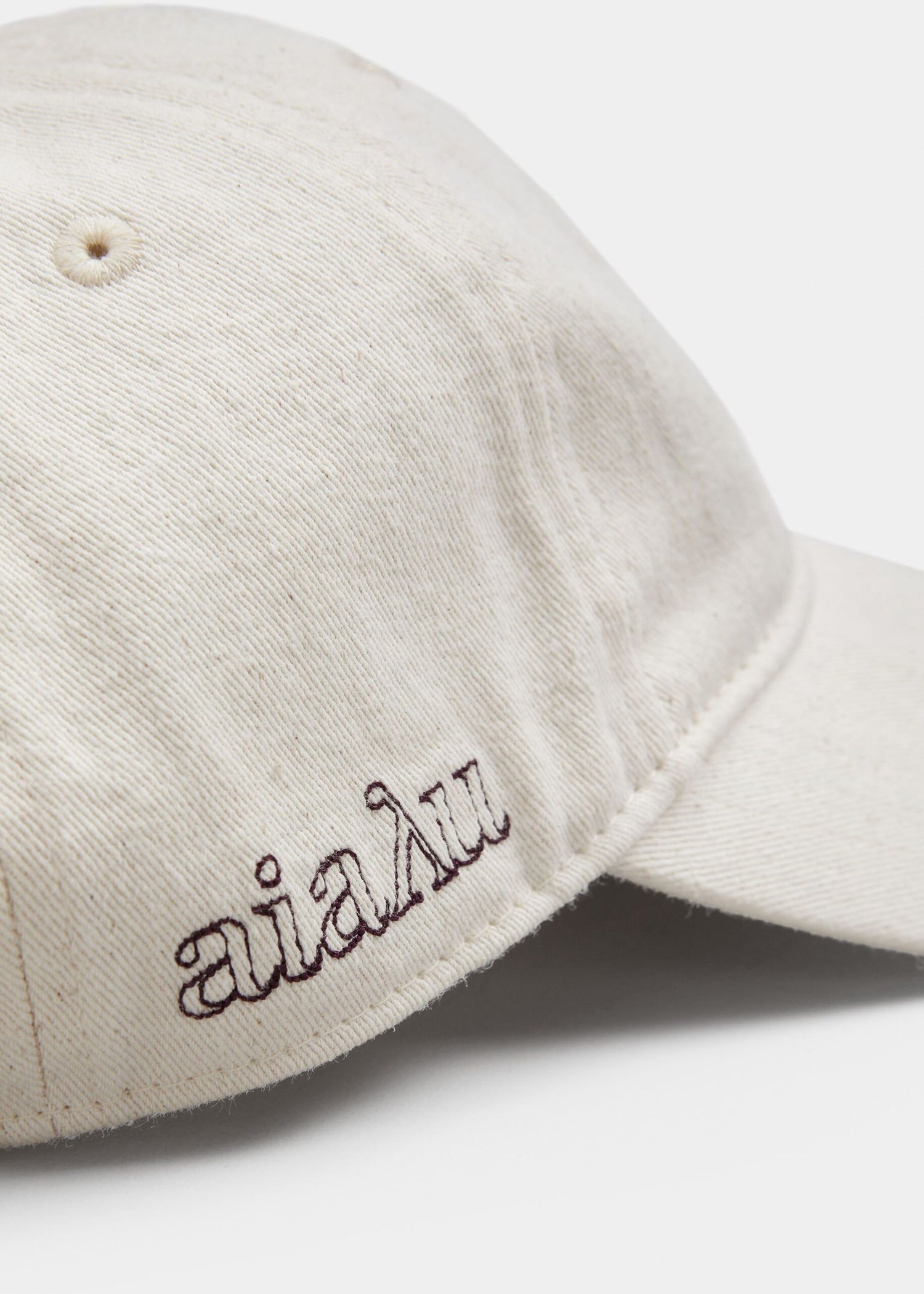 En off-white baseballkasket viser siden med "aialu" broderet i mørkt blæk, placeret mod en neutral baggrund.