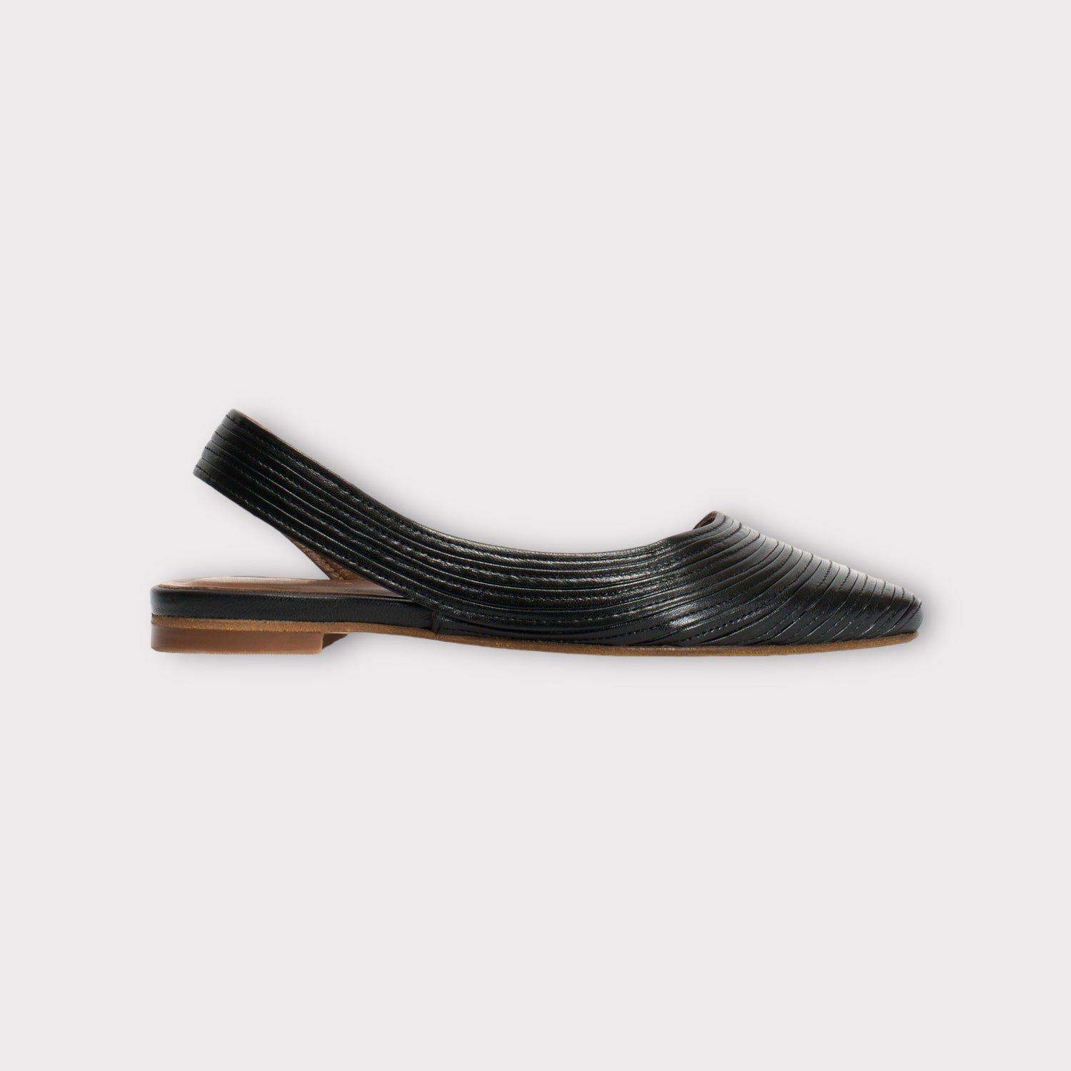 En sort damesko, en slingback flad, er vist på en hvid baggrund. Skoen er lavet af læder med riller.