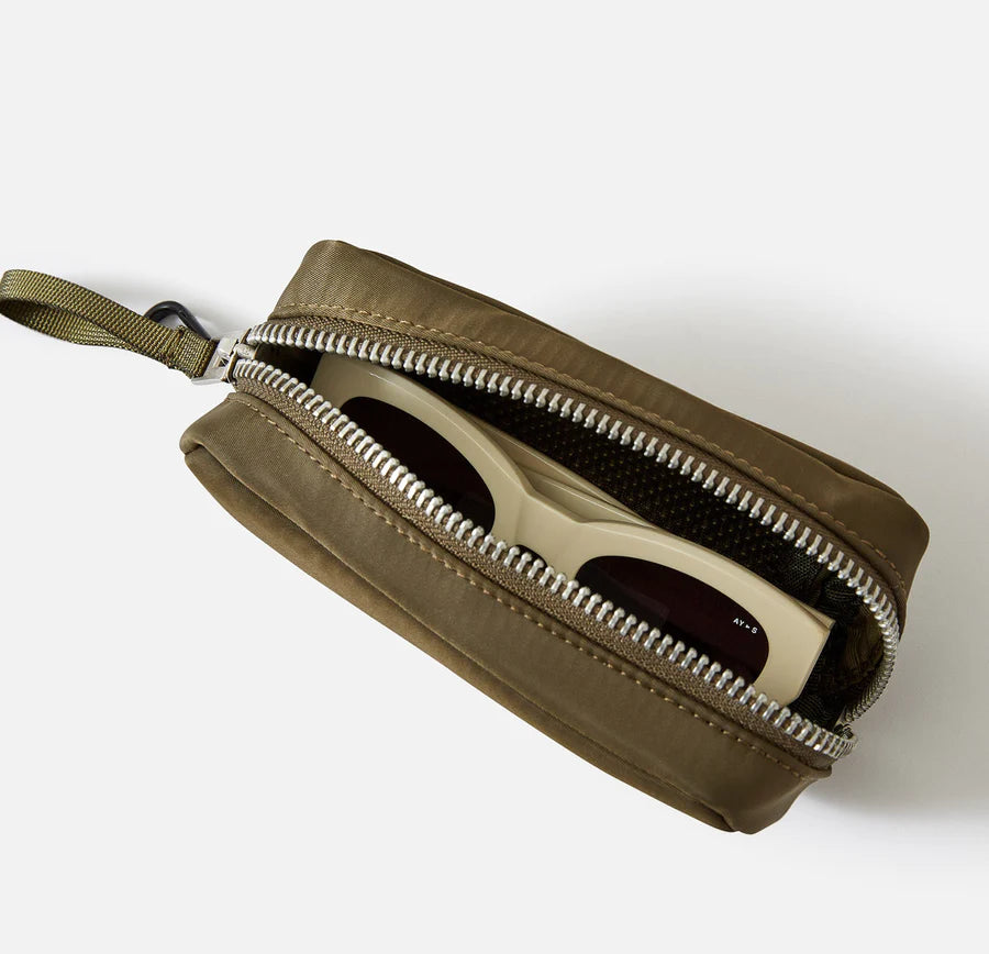 En olivengrøn taske med lynlås er delvist åben, og afslører et par lyse solbriller indeni. Tasken har en strop og en karabinhage. Baggrunden er hvid.