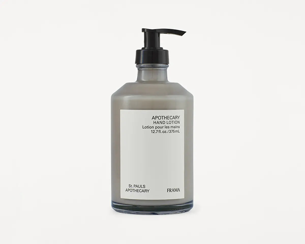 En grå lotionflaske med sort pumpe står på en hvid baggrund. Etiket på flasken læser: "APOTHECARY HAND LOTION, Lotion pour les mains, 12.7fl.oz./375mL, St. PAULS APOTHECARY, FRAMA."