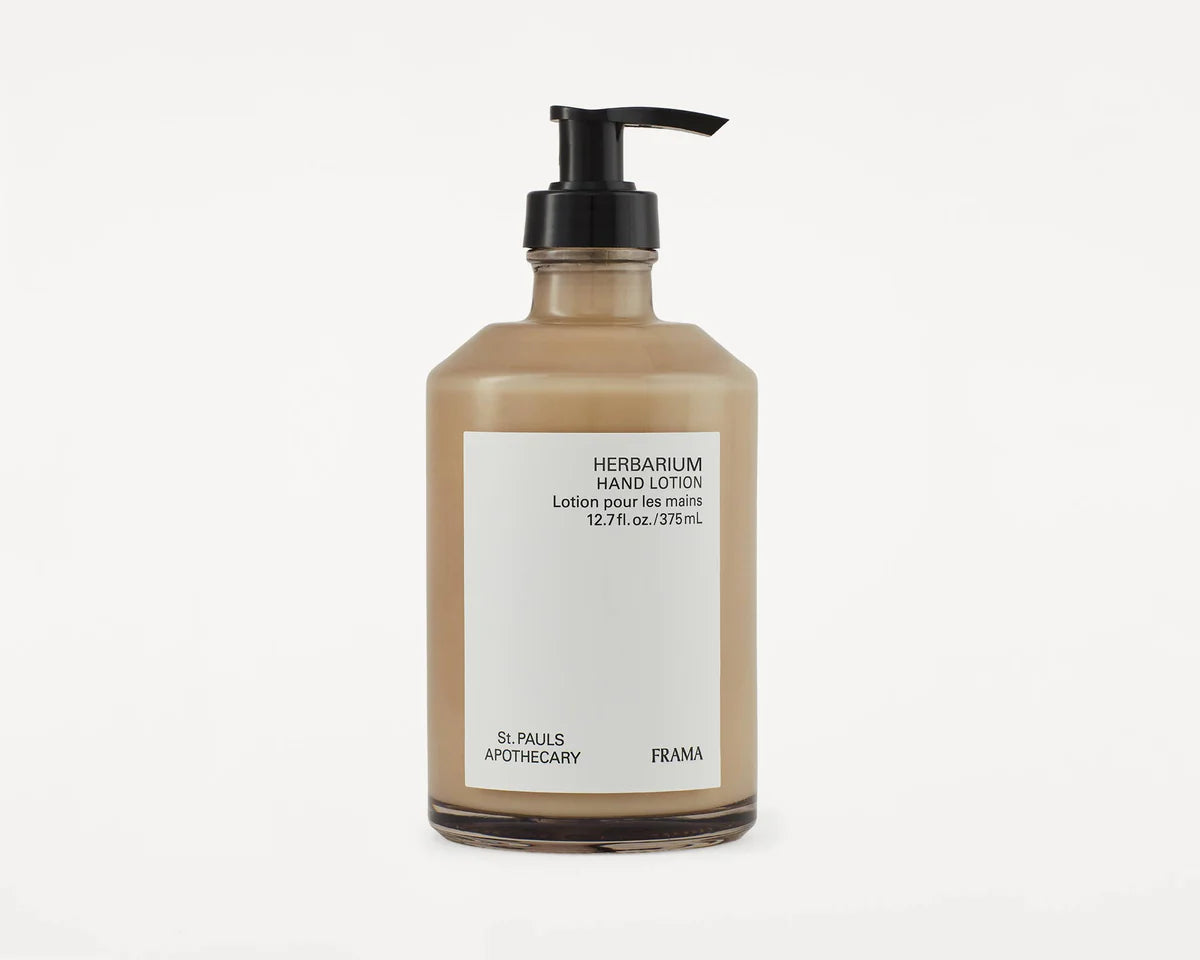 En beige lotionflaske med sort pumpehoved står på en hvid baggrund. Etiket viser "HERBARIUM HAND LOTION Lotion pour les mains 12.7 fl.oz./375 mL ST. PAULS APOTHECARY FRAMA".