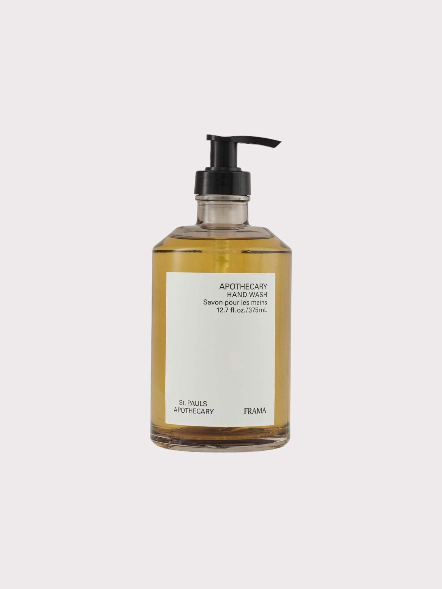 En flaske med håndvask står stille mod en hvid baggrund. Etiket på flasken læser: "APOTHECARY HAND WASH Savon pour les mains 12.7 fl. oz./375mL St. PAULS APOTHECARY FRAMA."