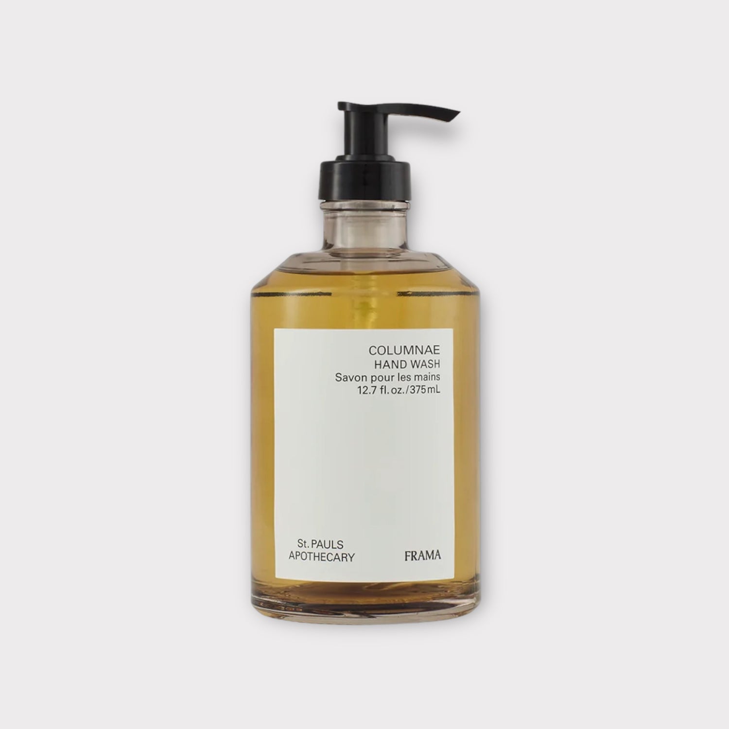 En glasflaske med håndsåbe "COLUMNAE HAND WASH, Savon pour les mains, 12.7 fl. oz./375mL" står stille. En sort pumpe er monteret ovenpå, og etiketter med "St. PAULS APOTHECARY FRAMA" er klistret på flasken, mod en hvid baggrund.