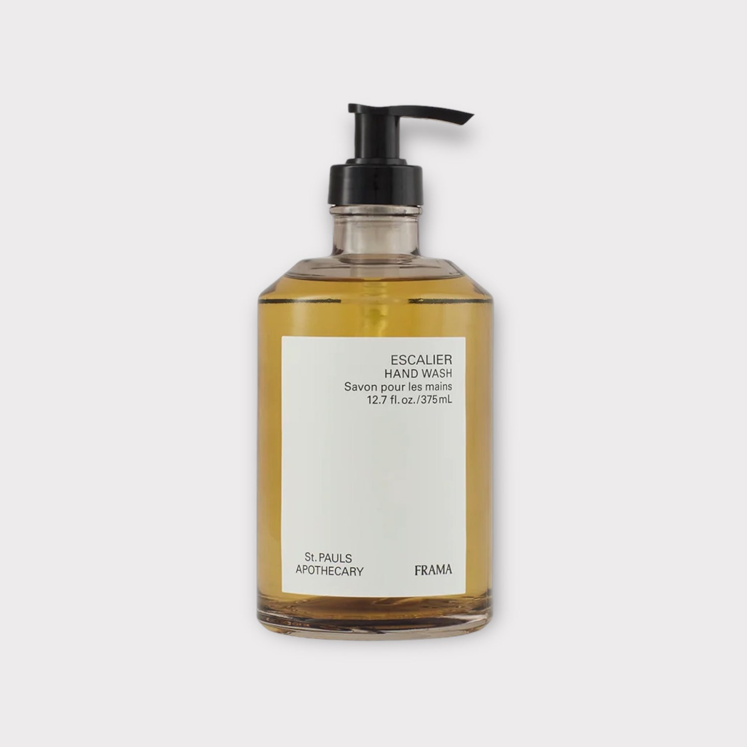 En flaske med håndvask står på en hvid baggrund. Etiketten på flasken siger: "ESCALIER HAND WASH Savon pour les mains 12.7 fl. oz./375mL St. PAULS APOTHECARY FRAMA".