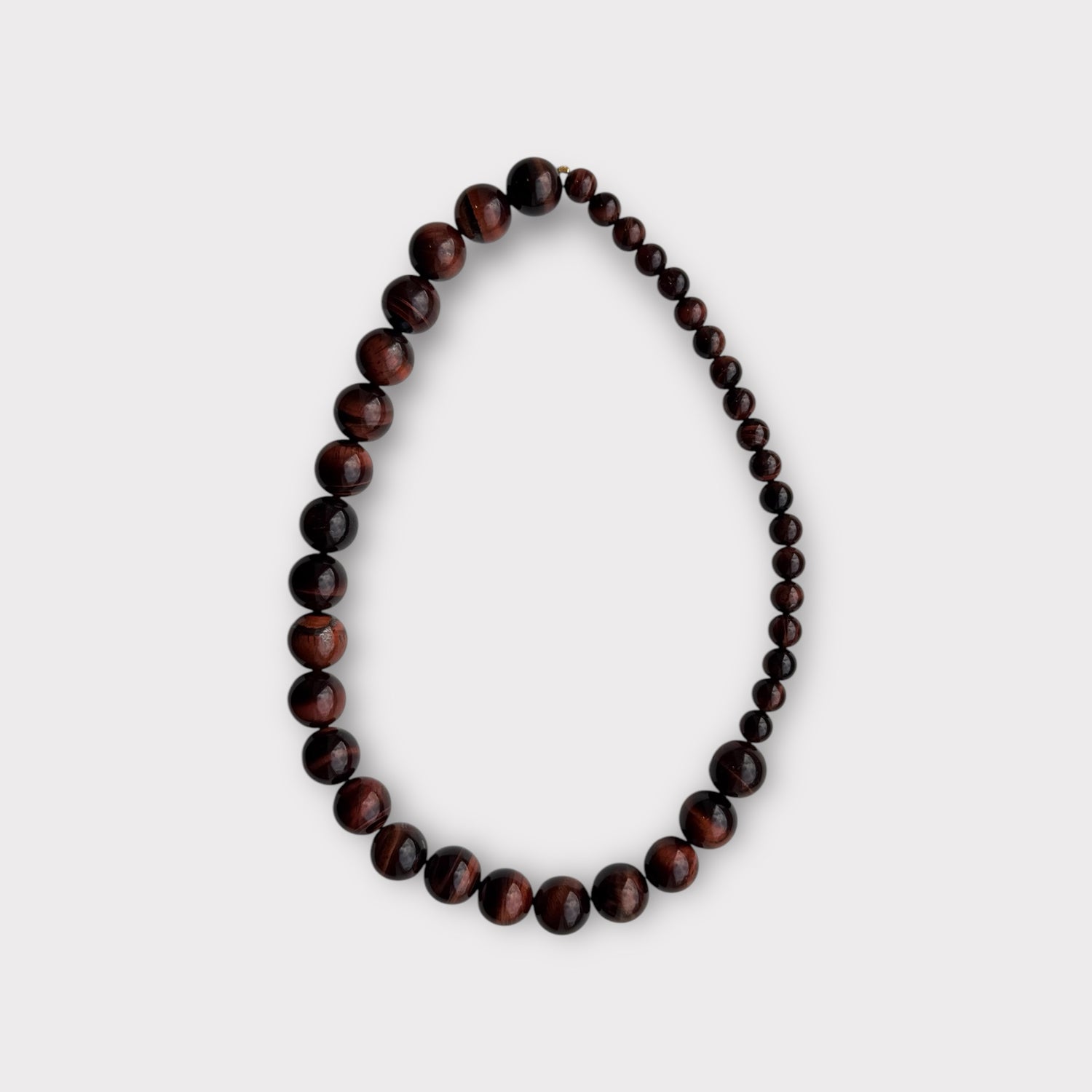 Et halskæde af runde, brunlige perler ligger i en løkke på en hvid baggrund, perlerne varierer i størrelse fra store til små.
