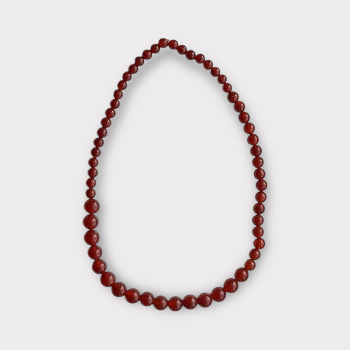 En halskæde af røde, runde perler ligger i en u-form på en hvid baggrund. Perlerne varierer i størrelse, med de største i midten.