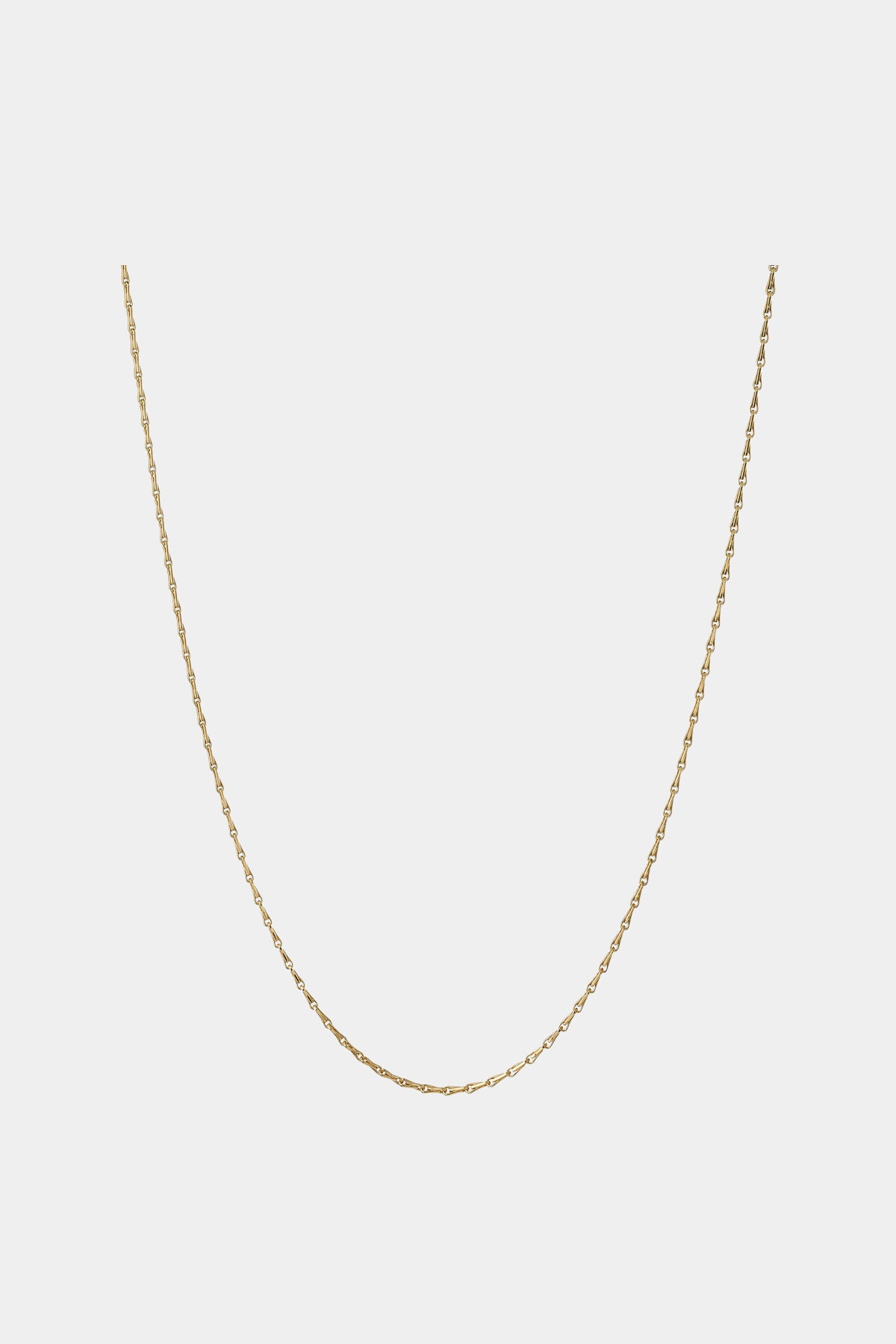 En guldkæde hænger nedad i et U-formet mønster mod en simpel, ensfarvet hvid baggrund. Kæden er fin og delikat i sit udseende.