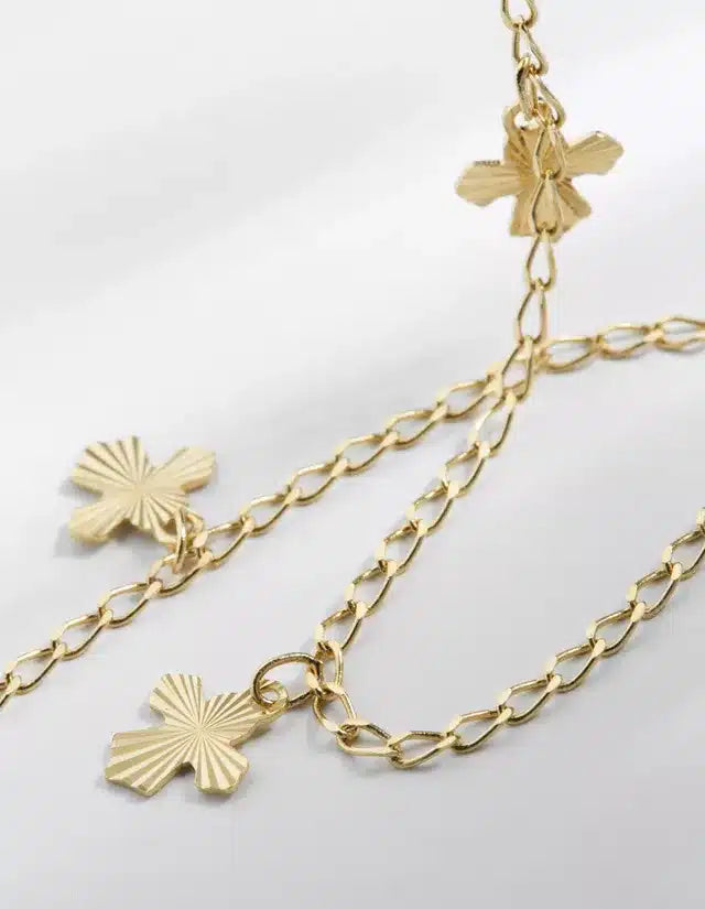 En guldkæde strækker sig diagonalt hen over en hvid overflade, med ornamenterede, gyldne kors placeret langs kæden som vedhæng.