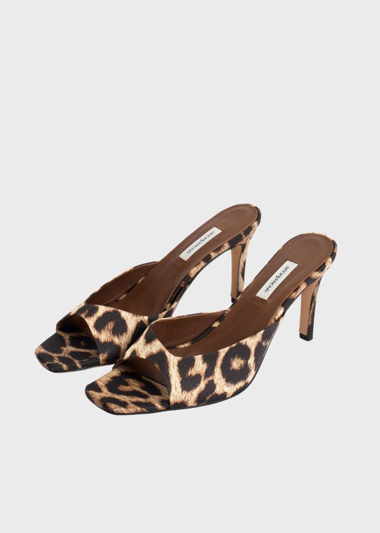 To leopardmønstrede højhælede sandaler med mærket "ANONYMOUS" ligger på en lysegrå overflade.