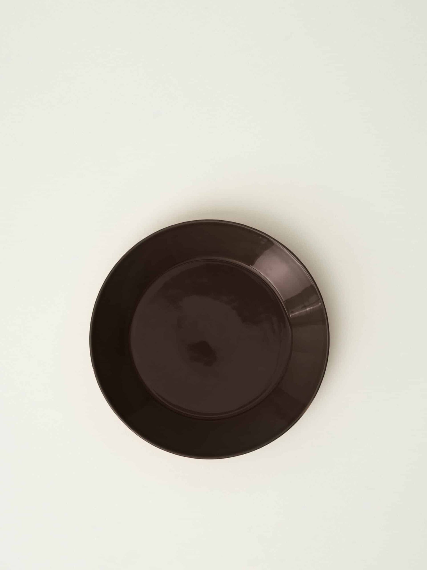 En brun tallerken hviler centreret på en lys, ensfarvet baggrund. Tallerkenen er rund og tom.