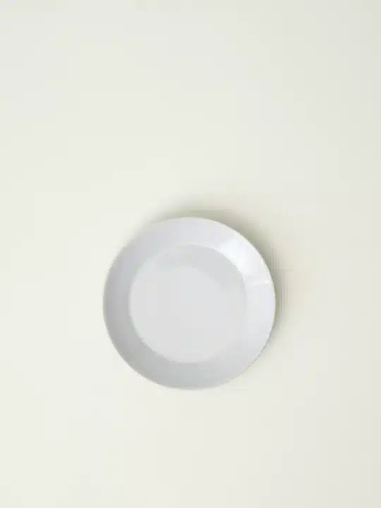 En hvid, tom tallerken hviler midt på en ensfarvet, cremefarvet overflade, muligvis et bord eller en baggrund.