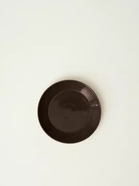 En brun tallerken ligger fladt på en hvid baggrund. Lys fremhæver den glatte overflade.