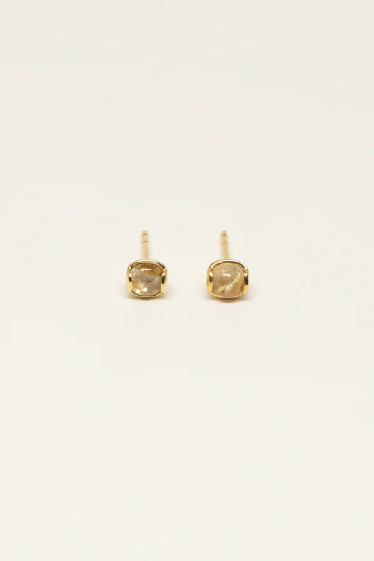 To gyldne øreringe med firkantede sten ligger side om side på en hvid overflade.