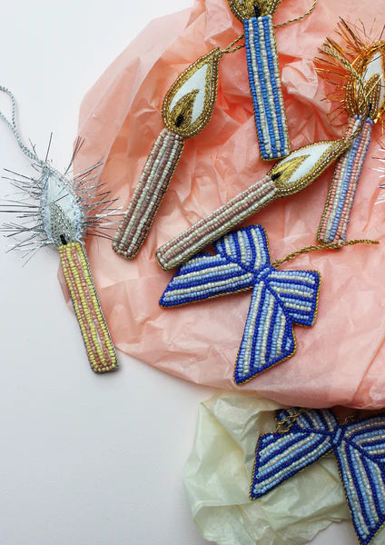 Beadsformede juleornamenter, inklusiv lys og sløjfer, ligger på et baggrundsmateriale af blød, krøllet papir. Ornamenterne har guld eller sølv tråd til ophæng.