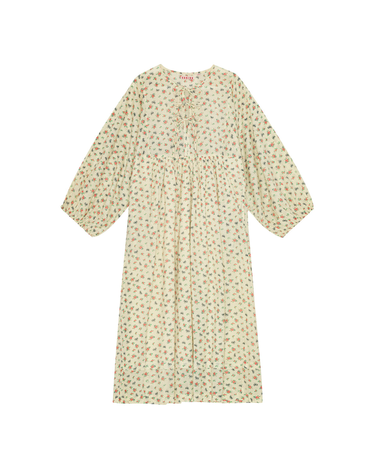 En kjole med blomster- og sløjfeprint er spredt ud. Kjolen har lange, blouson ærmer og snore ved halsudskæringen. Teksten "HABiBA" er synlig nær halsen.