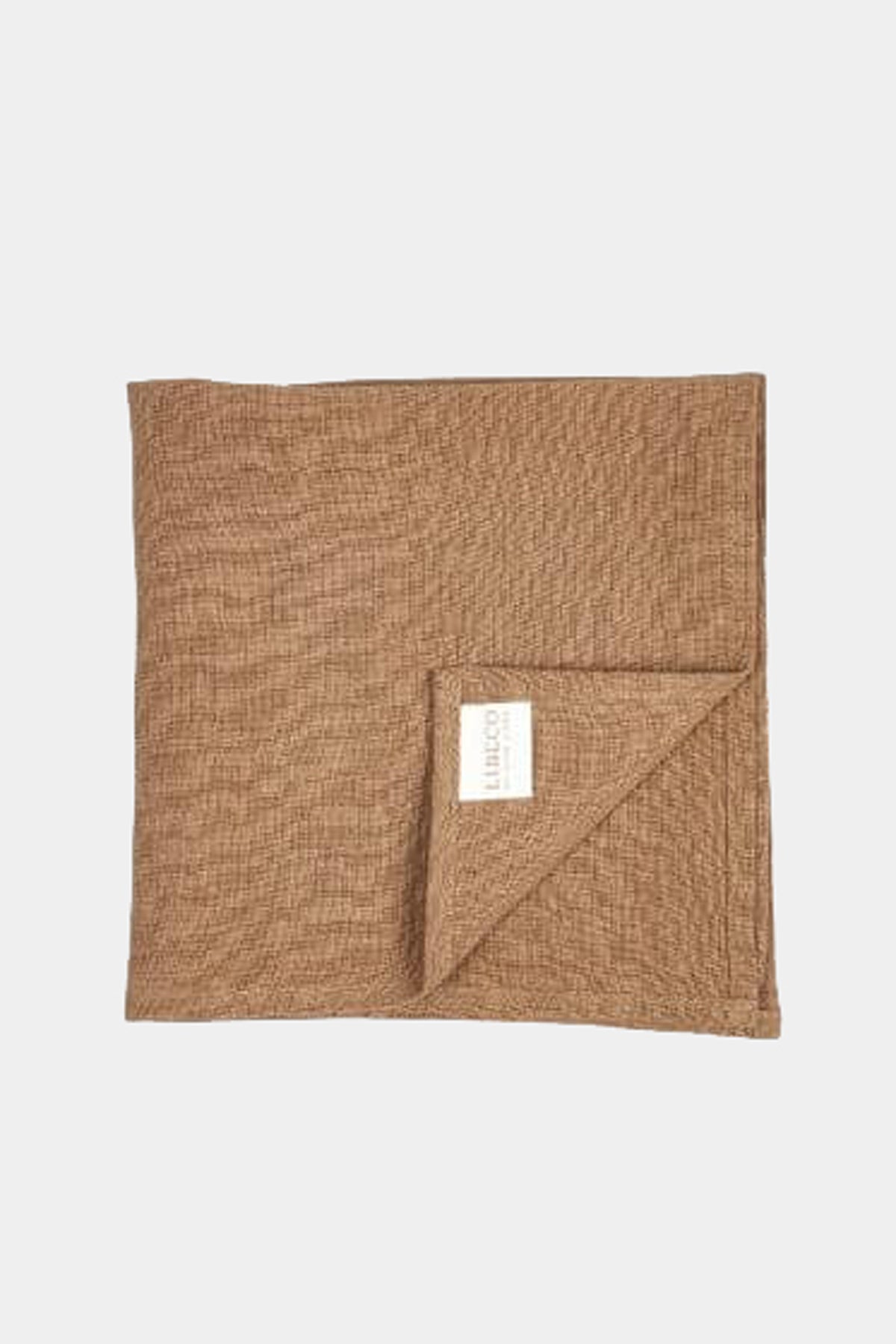 Et firkantet, brunt stof, der er foldet i hjørnet, ligger på en hvid baggrund. En hvid etiket med teksten "LIBECO HOME TEXTILES" er synlig på det foldede hjørne.