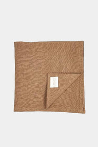 Et firkantet, brunt stof, der er foldet i hjørnet, ligger på en hvid baggrund. En hvid etiket med teksten "LIBECO HOME TEXTILES" er synlig på det foldede hjørne.
