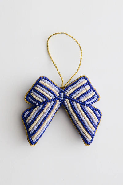 En blå og cremefarvet stribet sløjfe hænger fra en gylden snor mod en hvid baggrund. Sløjfen er lavet af perler med en gylden kant.
