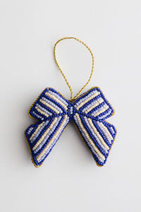 En blå og cremefarvet stribet sløjfe hænger fra en gylden snor mod en hvid baggrund. Sløjfen er lavet af perler med en gylden kant.