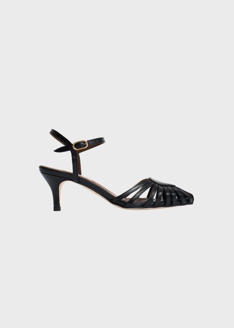 En sort lædersandal med hæl ses. Sandalen har en ankelrem med et guldspænde og et flettet design over tæerne. Den er placeret på en hvid baggrund.